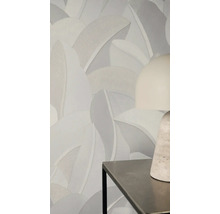 Vliesová tapeta s velkým strukturovaným vzorem listů v neutrálních šedých tónech na stěně za moderní stolní lampou.