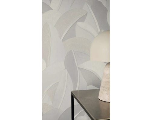 Vliesová tapeta s velkým strukturovaným vzorem listů v neutrálních šedých tónech na stěně za moderní stolní lampou.