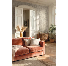 Světlý obývací pokoj s tapetou s motivem listů, parketami se vzorem rybí kosti, oranžovou sametovou pohovkou a dřevěnou komodou.