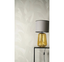 Vliesová tapeta s jemným vzorem listů za stolní lampou se žlutým skleněným podstavcem a šedým látkovým stínidlem na černém stolku.