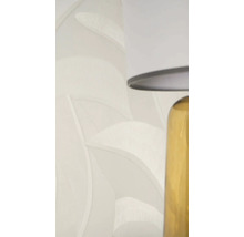 Vliesová tapeta se vzorem listů a texturou ve světle béžové barvě vedle stolní lampy.