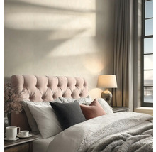 Světlá ložnice s prošívaným čelem postele, texturovaným povlečením, stolní lampou a stíny slunečního světla na zdi.