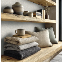 Strukturovaná nástěnná krytina ve světlém pokoji s dřevěnými policemi, keramikou, složenými dekami a polštáři v moderním přírodním stylu.