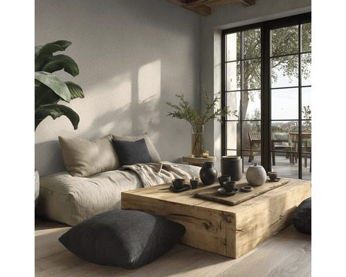 Světlý obývací pokoj s masivním dřevěným stolem, nízkou pohovkou, polštáři a velkými okny v minimalistickém stylu s přírodní úpravou stěn.