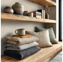 Nástěnná dekorace se strukturovanou vliesovou tapetou se vzhledem lnu, kombinovaná s policemi z masivního dřeva, keramikou a pletenými dekami.