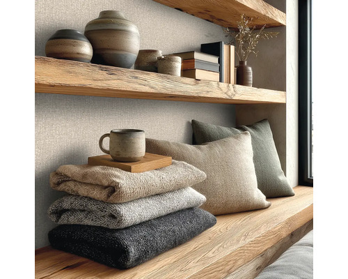 Nástěnná dekorace se strukturovanou vliesovou tapetou se vzhledem lnu, kombinovaná s policemi z masivního dřeva, keramikou a pletenými dekami.