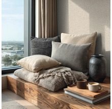 Útulný koutek u okna s dřevěnou lavicí, různými polštáři, vlněnou dekou, vázou a podnosem s šálky kávy na knihách.