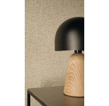 Moderní stolní lampa s černým kulatým stínidlem a dřevěným podstavcem před strukturovanou tapetou s tkaným vzorem.