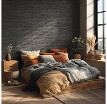 Ložnice s nástěnnou dekorací ve vzhledu kamene, dřevěnou postelí, textiliemi v zemitých tónech a jasným denním světlem z okna.