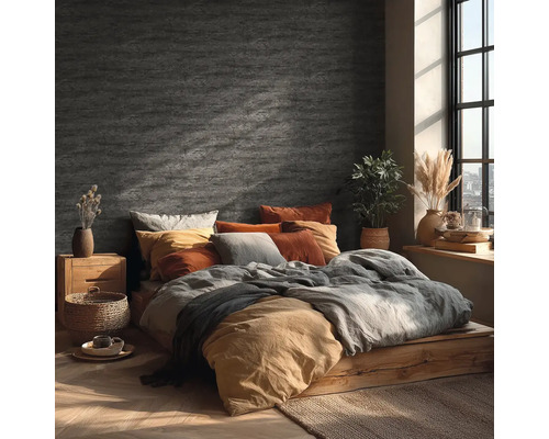 Ložnice s nástěnnou dekorací ve vzhledu kamene, dřevěnou postelí, textiliemi v zemitých tónech a jasným denním světlem z okna.