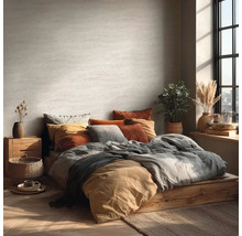 Světlá ložnice s postelí na dřevěném podstavci, mnoha polštáři a pokojovými rostlinami.