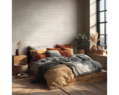 Světlá ložnice s postelí na dřevěném podstavci, mnoha polštáři a pokojovými rostlinami.