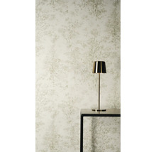 Vliesová tapeta s jemným vzorem stromů a lesa ve světlých odstínech za zlatou stolní lampou na černém stole.