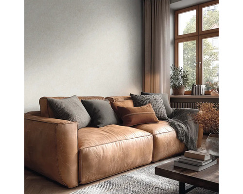 Světlá tapeta s jemnou texturou na stěně za hnědou koženou pohovkou v útulném obývacím pokoji s výhledem z okna.