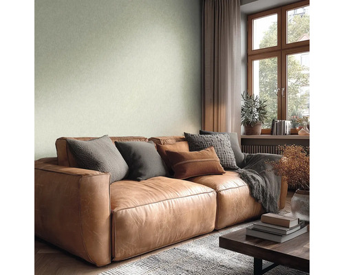 Obývací pokoj se strukturovanou světle zelenou tapetou, hnědou koženou pohovkou s polštáři, dřevěným oknem a světlou, útulnou atmosférou.