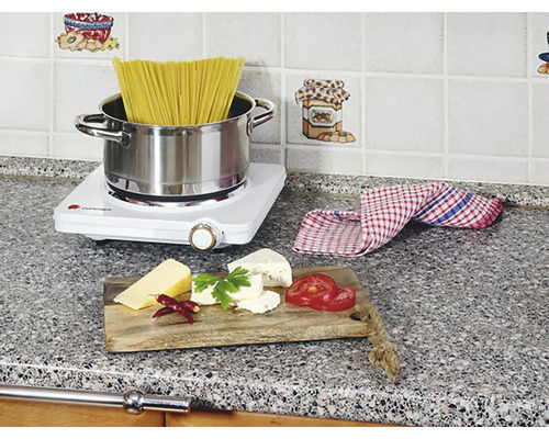 Scéna kuchyně s varnou deskou, těstovinami, sýrem a rajčaty na pracovní desce.