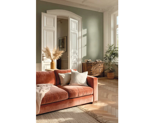 Světlý obývací pokoj se šalvějově zelenou stěnou, terakotovou sametovou pohovkou, dřevěnou komodou, parketami a velkou pokojovou rostlinou.