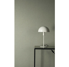 Strukturovaná vliesová tapeta v šedozelené barvě se vzhledem lnu, v kombinaci s bílou stolní lampou na černém kovovém stole.