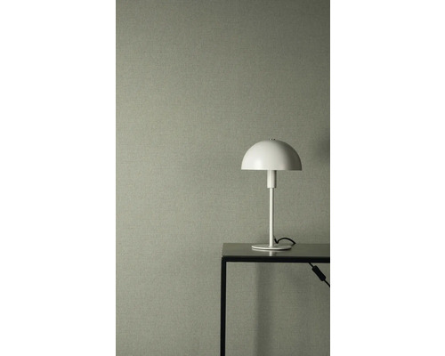 Strukturovaná vliesová tapeta v šedozelené barvě se vzhledem lnu, v kombinaci s bílou stolní lampou na černém kovovém stole.