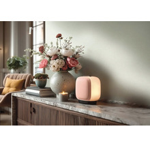 Moderní přenosná stolní lampa s růžovou přední částí a bílým světlem na mramorové komodě vedle vázy s květinami a svíčky.