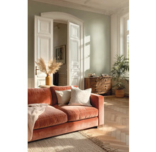 Světlý obývací pokoj se světle zelenou stěnou, rezavou sametovou pohovkou, parketami, jutovým kobercem a bílými křídlovými dveřmi.