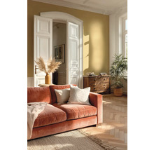 Světlý obývací pokoj s okrovou stěnou, oranžovou sametovou pohovkou, parketami v rybinovém vzoru, bílými křídlovými dveřmi a dřevěnou komodou.