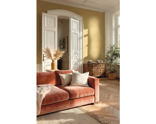 Světlý obývací pokoj s okrovou stěnou, oranžovou sametovou pohovkou, parketami v rybinovém vzoru, bílými křídlovými dveřmi a dřevěnou komodou.