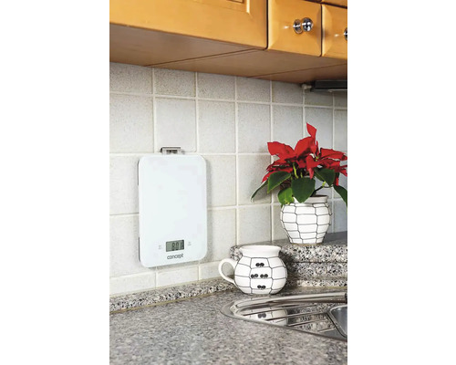 Bílá digitální kuchyňská váha na obkládané kuchyňské zdi