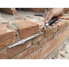 Řemeslník pracuje s cihlovou zdí s spárovací lžící