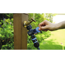 Zahradní kohoutek s rozdělovačem vody a připojenou zahradní hadicí v provozu.