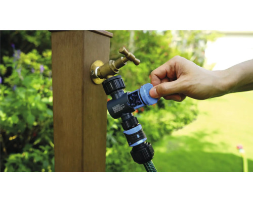 Zahradní kohoutek s rozdělovačem vody a připojenou zahradní hadicí v provozu.