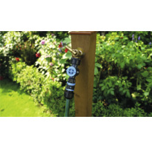 Zahradní scéna s vodovodním kohoutkem na dřevěném sloupku a připojenou zahradní hadicí