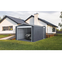 Moderní plechová garáž v tmavě šedé barvě s bílým rámem a čtyřkolkou uvnitř, na trávníku vedle bílého domu.