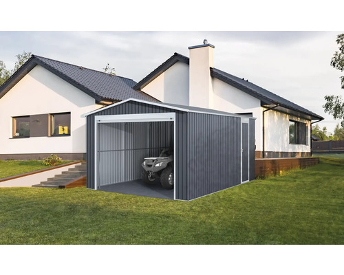 Moderní plechová garáž v tmavě šedé barvě s bílým rámem a čtyřkolkou uvnitř, na trávníku vedle bílého domu.