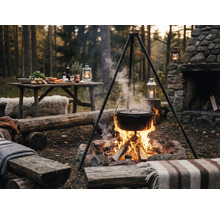 Venkovní scéna s trojnožkou, hrnec nad táborákem a stůl s ingrediencemi