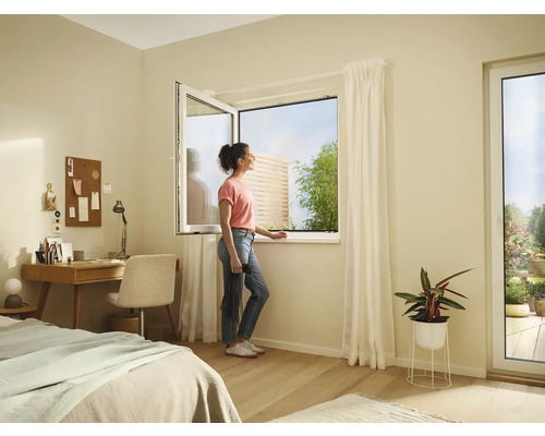 Světlá místnost s otevřeným oknem, psacím stolem, postelí a ženou, která se dívá z okna