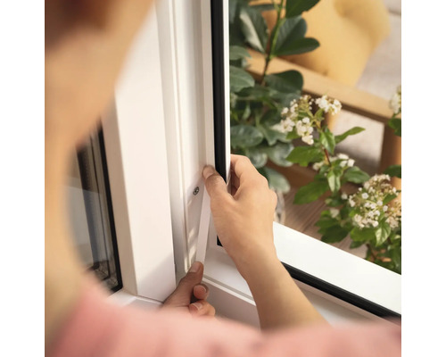 Osoba montuje okenní těsnění na bílý rám okna.