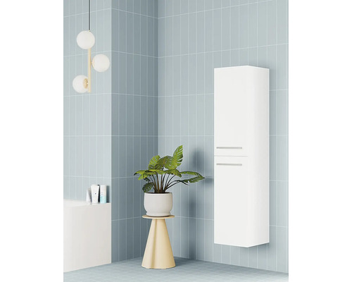 Vysoká, bílá závěsná koupelnová skříňka se dvěma úchyty v moderní koupelně se světle modrými obklady a pokojovou rostlinou.