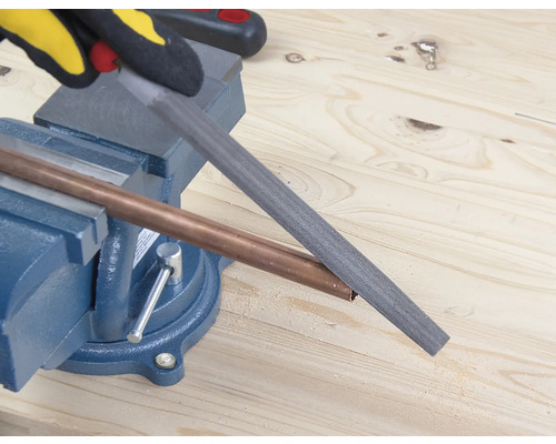 Měděná trubka opracovávaná pilníkem, který je upevněn ve svěráku.