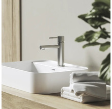 Moderní umyvadlová baterie ve vzhledu nerezové oceli na bílém umyvadle na desku, na dřevěné desce vedle ručníků ve světlé koupelně.