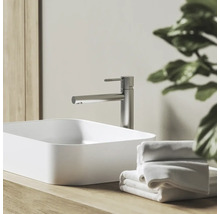 Moderní koupelna s vysokou pákovou baterií z kartáčovaného kovu a bílým obdélníkovým umyvadlem na dřevěné desce s ručníky.