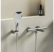 Moderní chromová sprchová souprava skládající se z hranaté ruční sprchy v nástěnném držáku a válcové sprchové baterie se sprchovou hadicí.