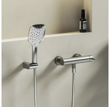 Moderní čtvercová ruční sprcha a válcová termostatická sprchová baterie z kovu na světlé stěně.