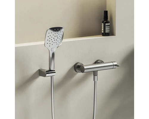 Moderní čtvercová ruční sprcha a válcová termostatická sprchová baterie z kovu na světlé stěně.