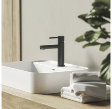 Černá matná umyvadlová baterie na bílém umyvadle na desku na dřevěném podkladu v koupelně s ručníky.