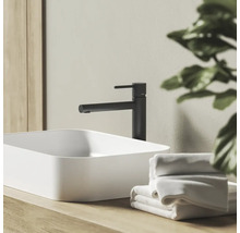 Moderní koupelnová scéna s černou pákovou umyvadlovou baterií a bílým umyvadlem na desku na dřevěném podkladu s ručníky.