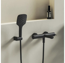 Moderní sprchový set v matně černé barvě s obdélníkovou ruční sprchou a válcovou nástěnnou baterií v minimalistické koupelně.