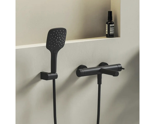 Moderní sprchový set v matně černé barvě s obdélníkovou ruční sprchou a válcovou nástěnnou baterií v minimalistické koupelně.
