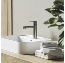 Umyvadlová baterie ve vzhledu nerezové oceli na bílém umyvadle na desku, s dřevěnou deskou a bílými ručníky.