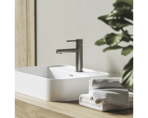 Umyvadlová baterie ve vzhledu nerezové oceli na bílém umyvadle na desku, s dřevěnou deskou a bílými ručníky.